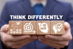 Person holding wooden blocks with icons representing strategy, focus, thought, and verification, with the text 'Think Differently'.