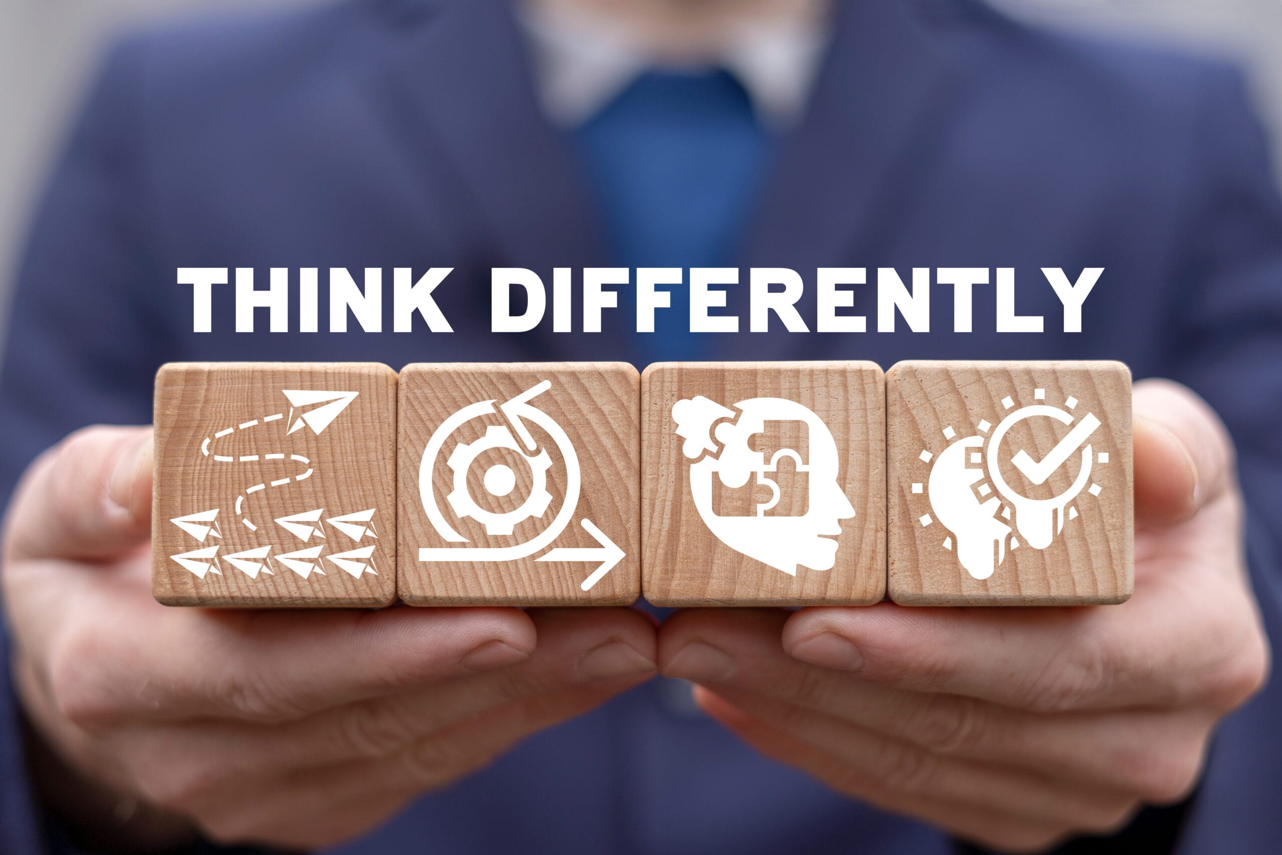 Person holding wooden blocks with icons representing strategy, focus, thought, and verification, with the text 'Think Differently'.