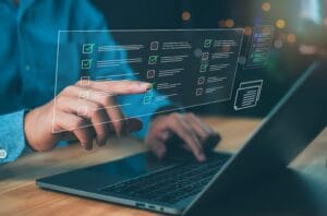 A person using a laptop with a digital checklist displayed on the screen, showing checked and unchecked items.